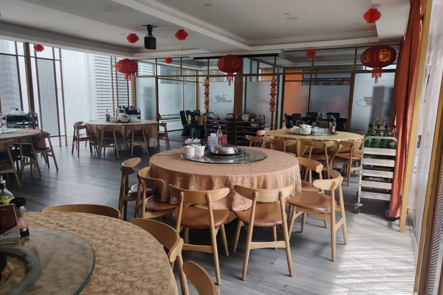 The back hall set with round banquet tables under red lanterns, projector screen at the far end.
