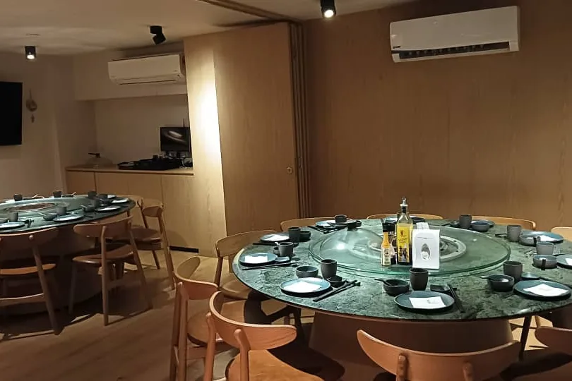 A private room with two round green-marble tables, timber panelling and a wall-mounted screen.